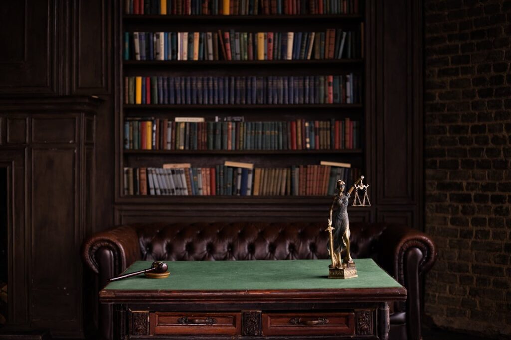 pexels-photo-6077091 A classic study room with shelves of books, a gavel, and Lady Justice figurine on a green table.